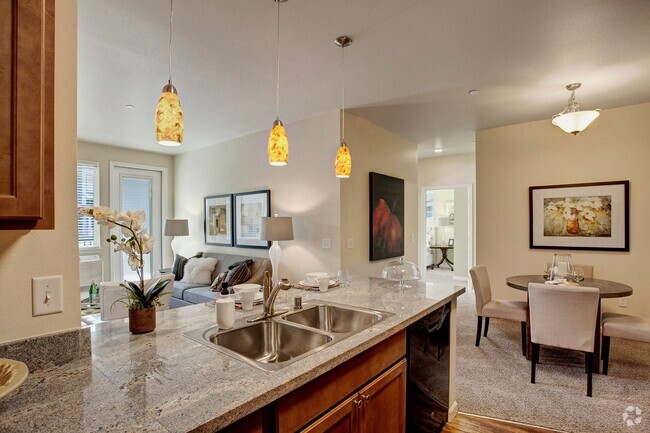 A kitchen with our sleek appliances and stone countertops with a view into the dining area and living room