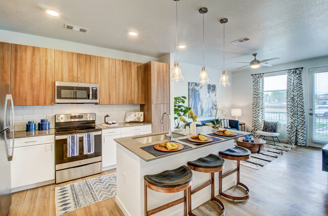 Kitchens feature oak upper and white lower cabinetry, grey quartz countertops, white subway tile backsplash, kitchen island or breakfast bar, and luxury vinyl plank flooring - Avalon Flatirons