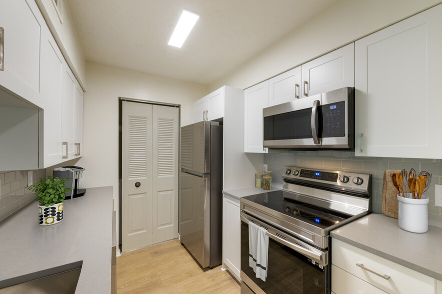 Renovated Meadows II kitchen with stainless steel appliances, white cabinetry, grey quartz countertops, grey tile backsplash, and hard surface flooring - Avalon Fairway Hills-Meadows