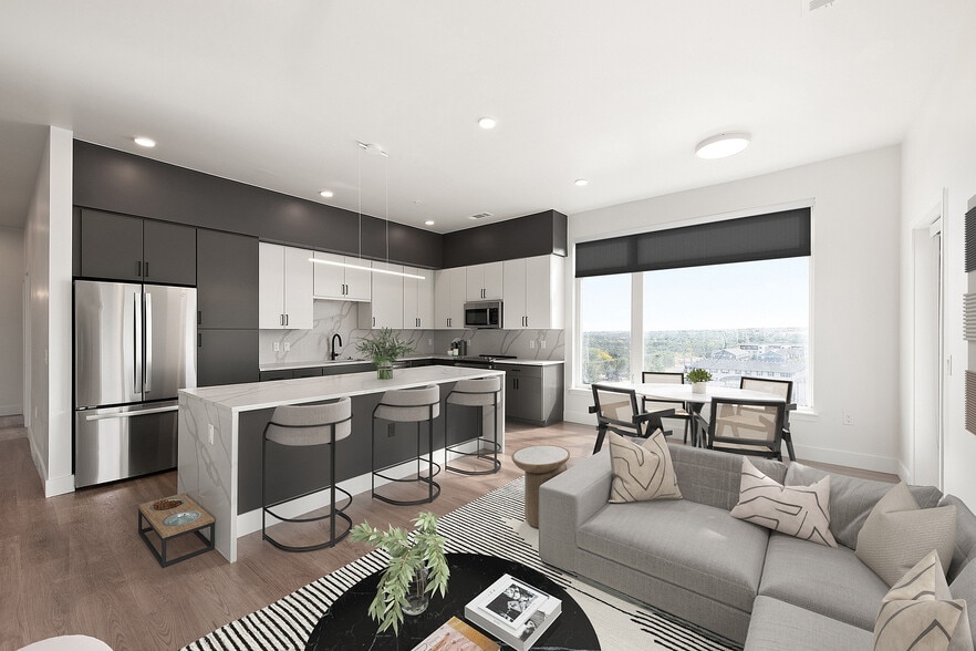 Modern open-plan kitchen and living area featuring sleek cabinetry, stainless steel appliances, a spacious island with bar seating, and stylish decor, enhanced by large windows offering scenic views. - Dorian