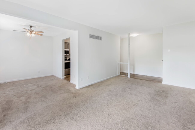Inviting living room with plush carpeting, classic fireplace, and natural light streaming through large windows. - Woods Mill Park Apartments & Townhomes