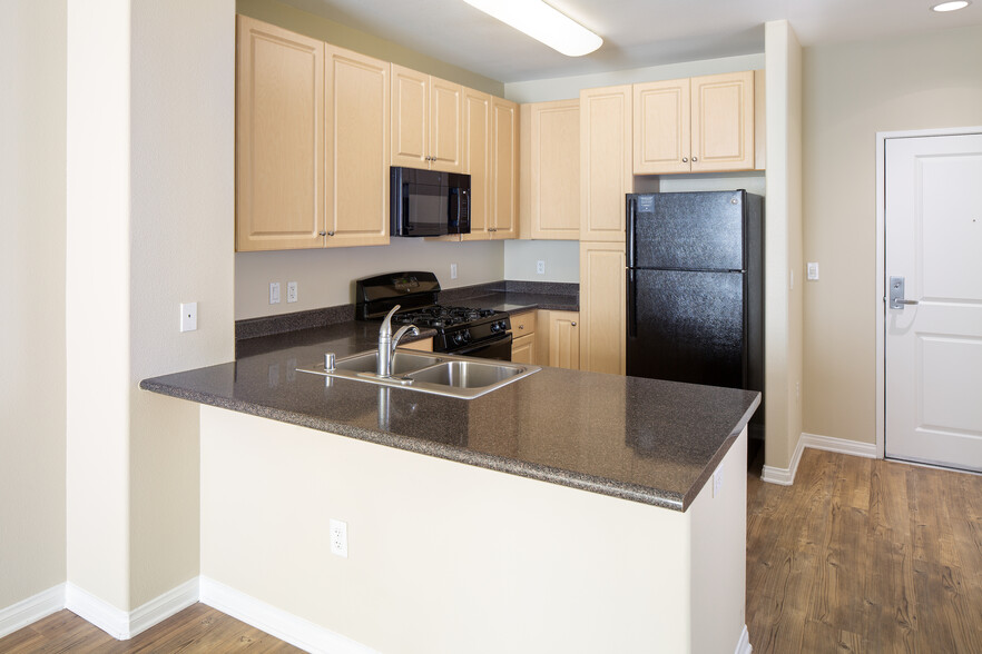 Kitchen with oak cabinetry, grey countertops, black appliances, and hard surface flooring - Avalon Warner Place