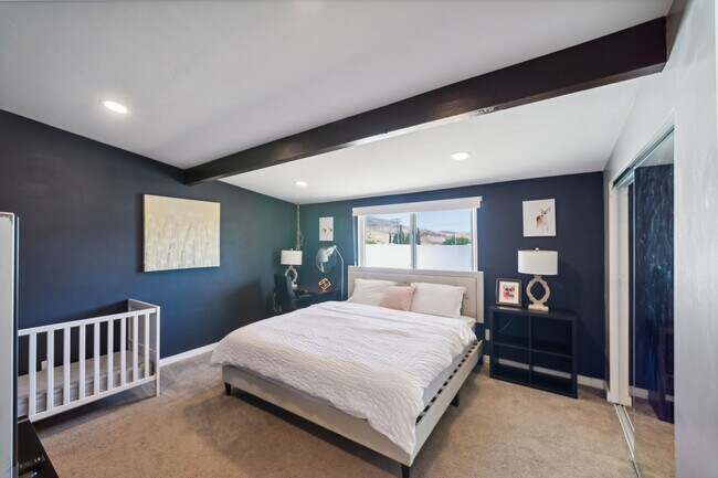Enjoy a comfortable bedroom featuring a king bed, baby crib, workspace, and smart TV - 9853 Saint George St