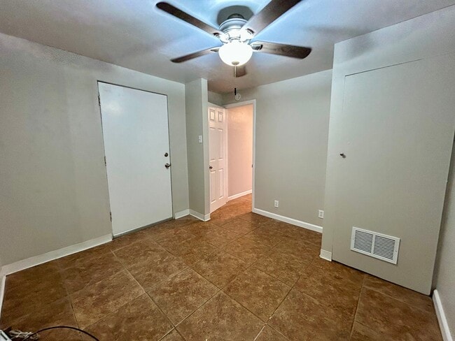 Bright room with neutral walls, a ceiling fan, tiled flooring, and a door leading to a hallway. - Boardwalk Apartments