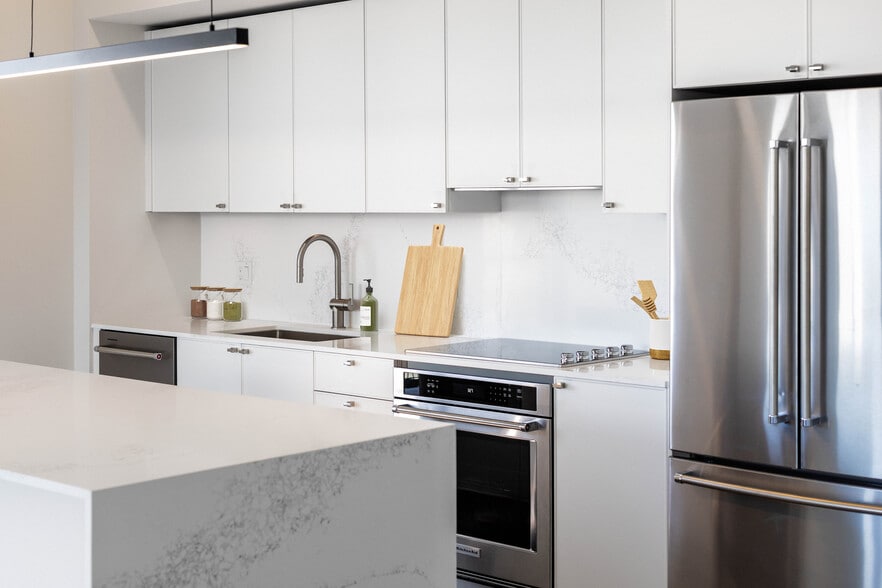 Signature Collection kitchen with white cabinetry, white marbled quartz countertop and backsplash, wine fridge, and upgraded stainless steel appliances - Avalon South Miami