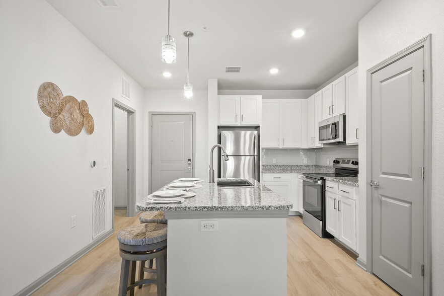 Modern kitchen interior with sleek granite countertops, stainless steel appliances, and stylish bar seating. Bright and inviting space perfect for culinary creativity. - Avana Parkway