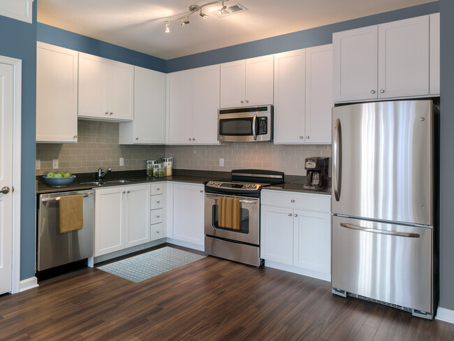 Kitchen with quartz stone countertop, white cabinetry, tile backsplash, stainless steel appliances and hard surface flooring. - Avalon Arlington North