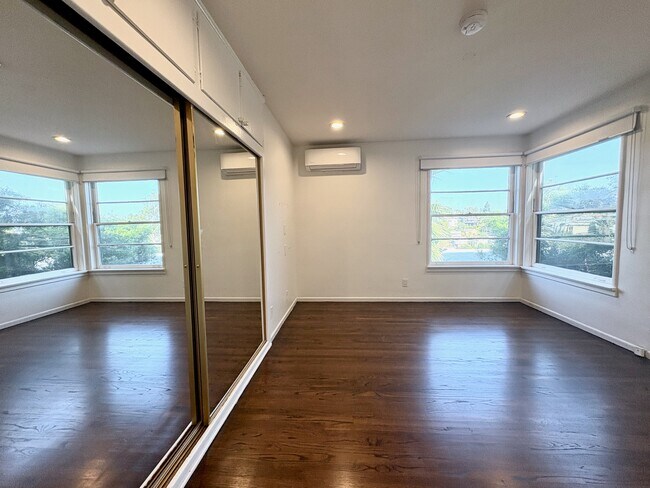Master bedroom with generous mirrored built-in wardrobes, large windows, and leafy views. - 1672 Rotary Dr