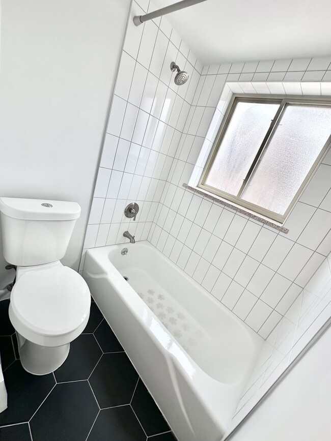 Modern bathroom featuring a sleek white bathtub, elegant geometric floor tiles, and a bright window for natural light. - Columbine Plaza