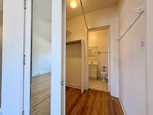 Bright hallway leading to a cozy bathroom with elegant hardwood flooring and a spacious mirror. - Ivanhoe