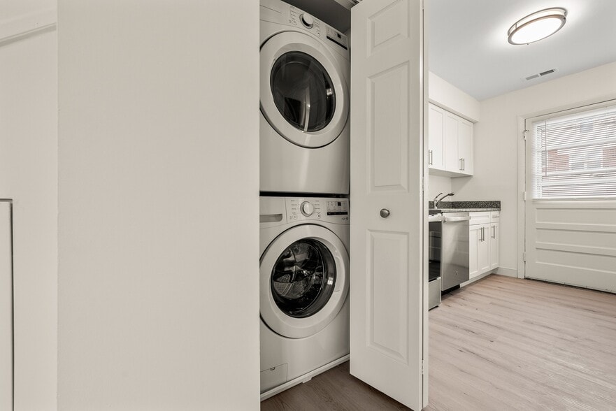 Modern apartment interior with a sleek stackable washer and dryer set in a closet next to a bright kitchen featuring white cabinets - Stony Brook Commons