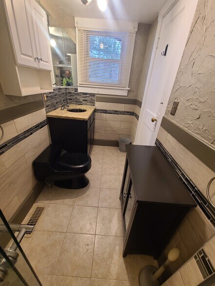 Tiled bathroom features granite countertop with black oval sink and Kohler black one piece toilet. - 122 Edgerton Rd