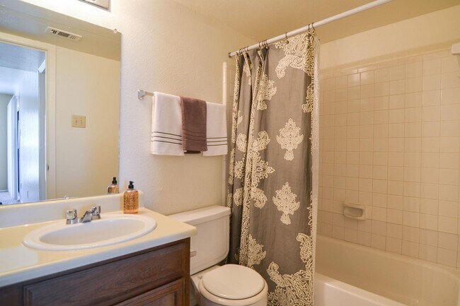 A bathroom with a tub, cabinet storage, and a wide mirror over the sink - Wildflower