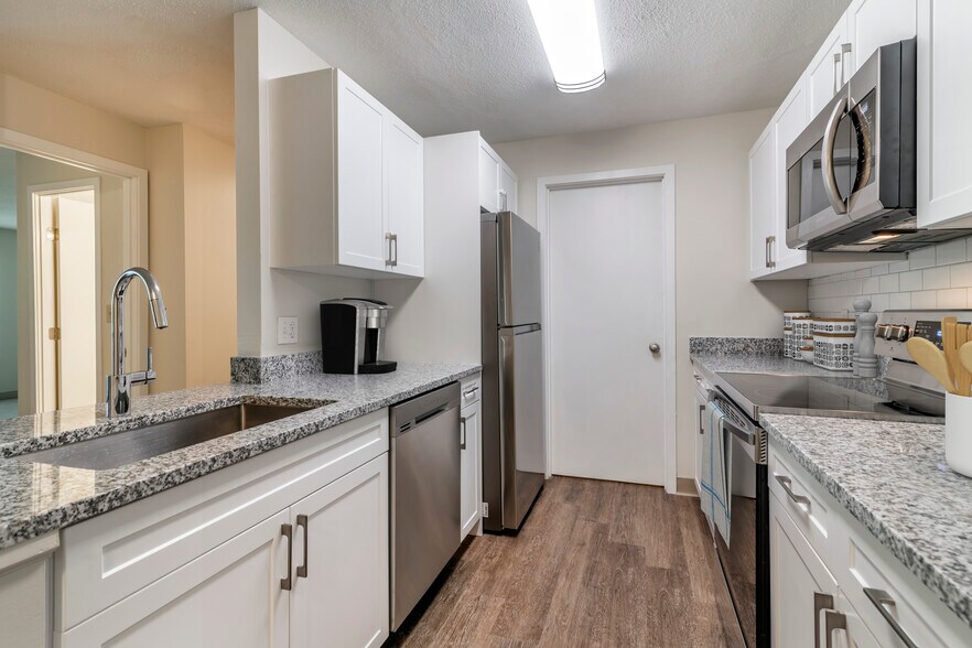 Renovated Package I kitchen with stainless steel appliances, grey speckled granite countertops, white cabinetry, white tile backsplash, and hard surface flooring - eaves Burlington
