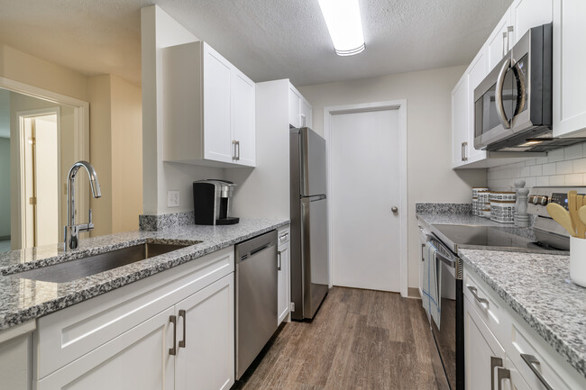 Renovated Package I kitchen with stainless steel appliances, grey speckled granite countertops, white cabinetry, white tile backsplash, and hard surface flooring - eaves Burlington