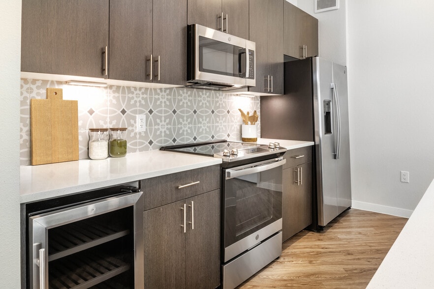 Kitchens with stainless steel appliances, wine fridges, quartz countertops, tile backsplash, and hard surface flooring - Avalon Townhomes Bee Cave