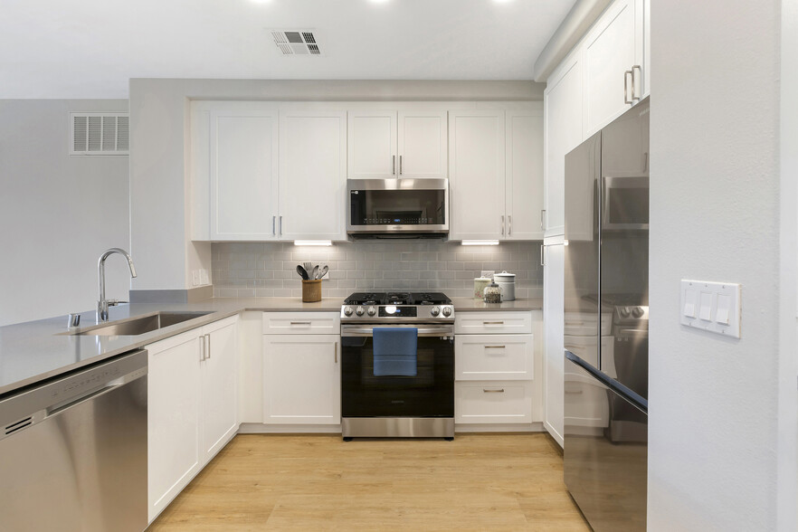 Renovated Package I kitchen with stainless steel appliances, grey quartz countertops, white cabinetry, grey tile backsplash, and hard surface flooring - Avalon Encino