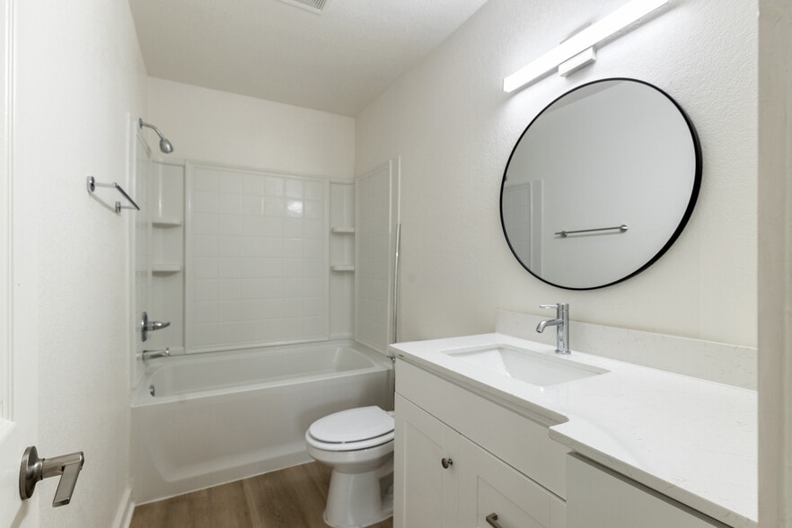 Modern bathroom featuring sleek white cabinetry, elegant round mirror, and pristine bathtub with contemporary fixtures. - Pointe at North Penn