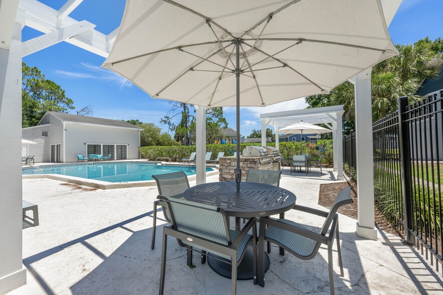 Inviting outdoor pool area featuring comfortable seating under umbrellas, modern grill, and lush greenery, perfect for relaxation and entertaining. - Vista North