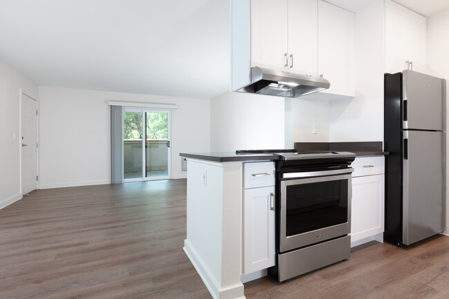 Living area with balcony access and kitchen with white cabinetry, dark grey countertops, stainless steel appliances and hard surface flooring - eaves Fremont