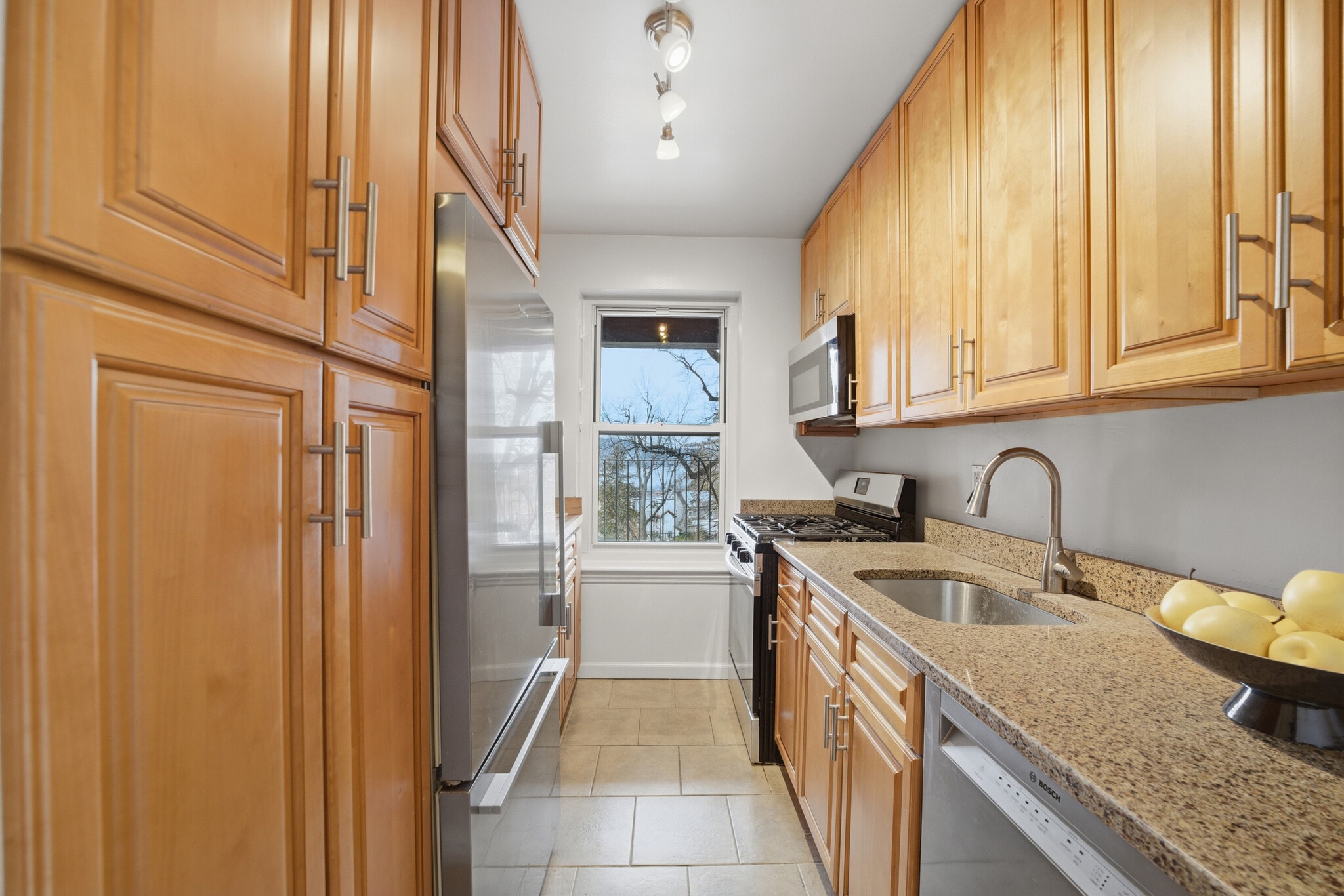 Kitchen featuring stainless steel appliances, wood cabinetry and light stone countertops - 555 Broadway