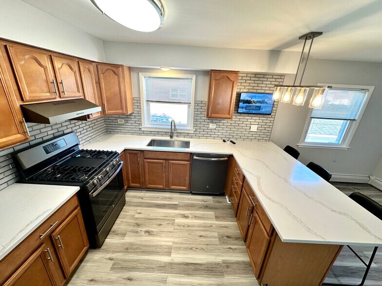 Peninsula kitchen with quartz counters and three counter chairs. - 671 56th St
