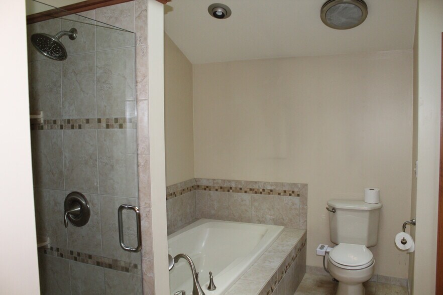 Tiled primary bathroom with a separate glass-door shower and deep soaking tub. - 6235 Sunnywood Dr