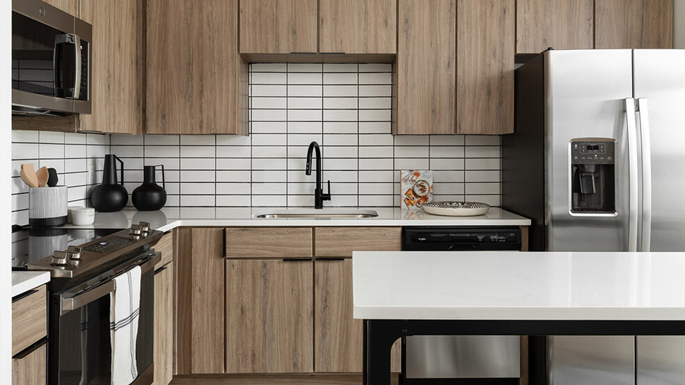 Apartment kitchen with stainless steel appliances, quartz countertops and wood-style flooring. - Griffis at The Domain