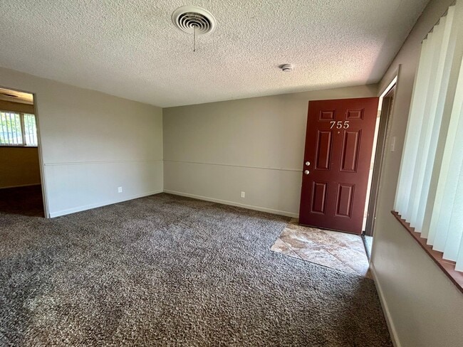 Inviting living space with plush carpeting, neutral walls, and natural light streaming through large windows, enhancing the cozy ambiance. - Boardwalk Apartments