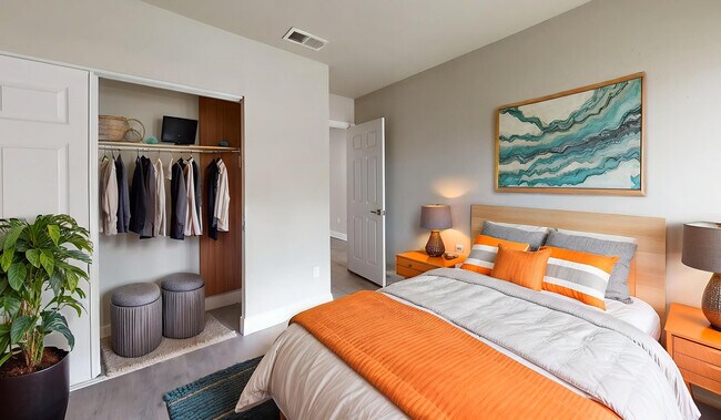 Bright and inviting bedroom with a modern design, featuring a cozy bed with orange accents, an open closet neatly organized, and stylish decor. - Soto Apartments