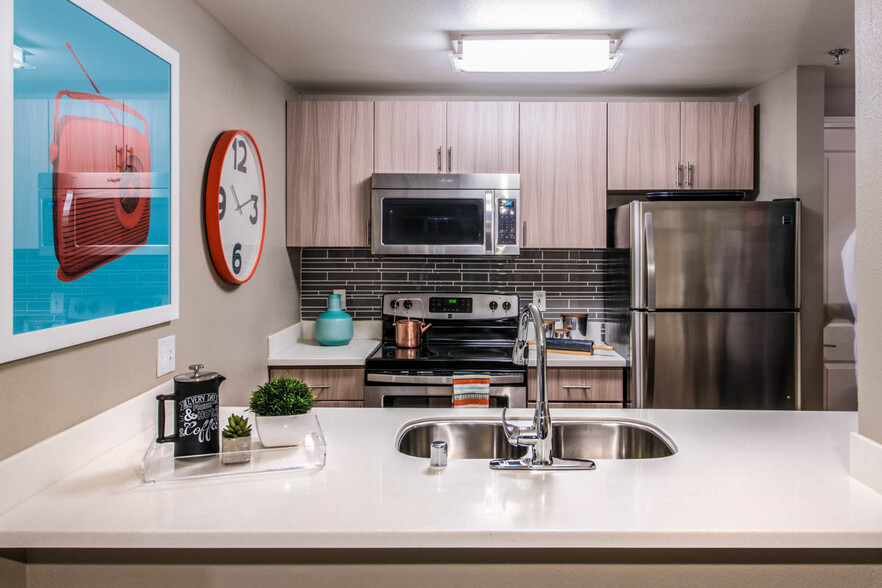 Apartment kitchen with stainless steel appliances, quartz countertops and wood-style flooring. - Griffis Belltown