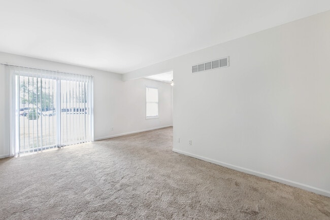 Bright and airy living room with plush carpeting and large sliding glass doors leading to outdoor space. - Woods Mill Park Apartments & Townhomes