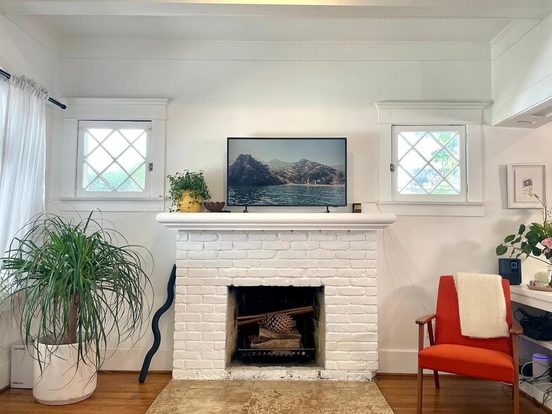 Bright living room with original hardwood floors, and a decorative fireplace. - 6000 Carlton Way