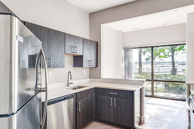 Modern kitchen with sleek dark wood cabinets, stainless steel appliances, and a large window overlooking a scenic outdoor view.