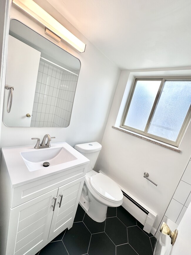 Bright, modern bathroom with hexagonal tile floor, sleek vanity, and large window for natural light. - Columbine Plaza