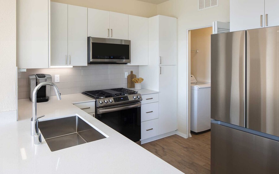 Renovated Package I kitchen featuring white cabinetry, white quartz countertops, stainless steel appliances, and hard surface flooring. In-unit laundry with full sized washer and dryer - Avalon Simi Valley