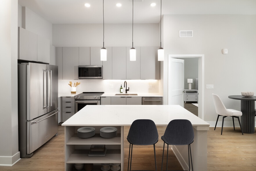 Signature Collection kitchen with stainless steel appliances, light grey cabinetry, marbled quartz countertops and backsplash, under-cabinet lighting, built-in shelves, and hard-surface flooring - Avalon at Becker Farm