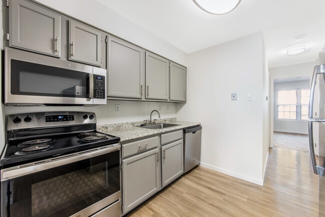 Modern kitchen with sleek stainless steel appliances, spacious grey cabinetry, and elegant granite countertops. - Woods Mill Park Apartments & Townhomes
