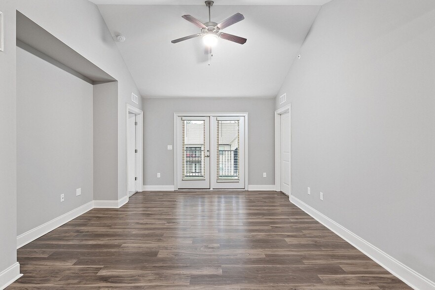 Bright and spacious living area with elegant wooden flooring, modern ceiling fan, and double doors leading to a balcony. - Grove Park