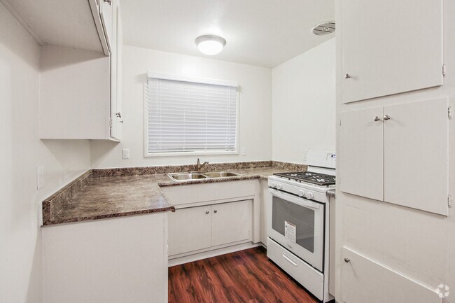 Kitchen with granite countertops, white gas range, white cabinets, and wood style flooring - Glen Haven Apartments