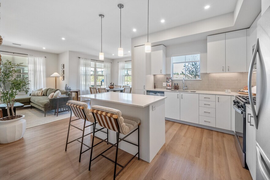Finish Package I kitchen with stainless steel appliances, white cabinetry, grey tile backsplash, white quartz countertops, and hard surface flooring - Avalon Parker