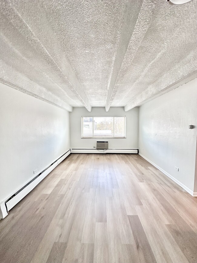 Bright and spacious room with modern wood flooring and large window inviting natural light. - Columbine Plaza