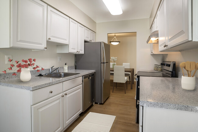 Renovated Package I kitchen featuring stainless steel appliances, white cabinetry, grey laminated countertops, and hard surface flooring - eaves Tysons Corner