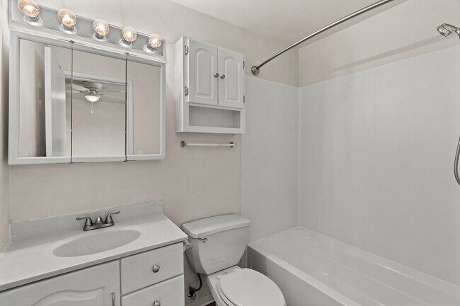 Clean and bright bathroom featuring a full tub, spacious vanity, and extra cabinet storage. - Highland Court Apartments