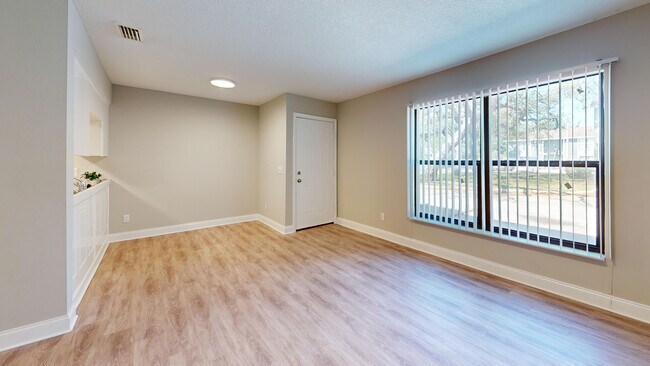 Bright and inviting living room with large windows and elegant wood flooring, ideal for relaxation and entertaining. - Chateau of Tampa