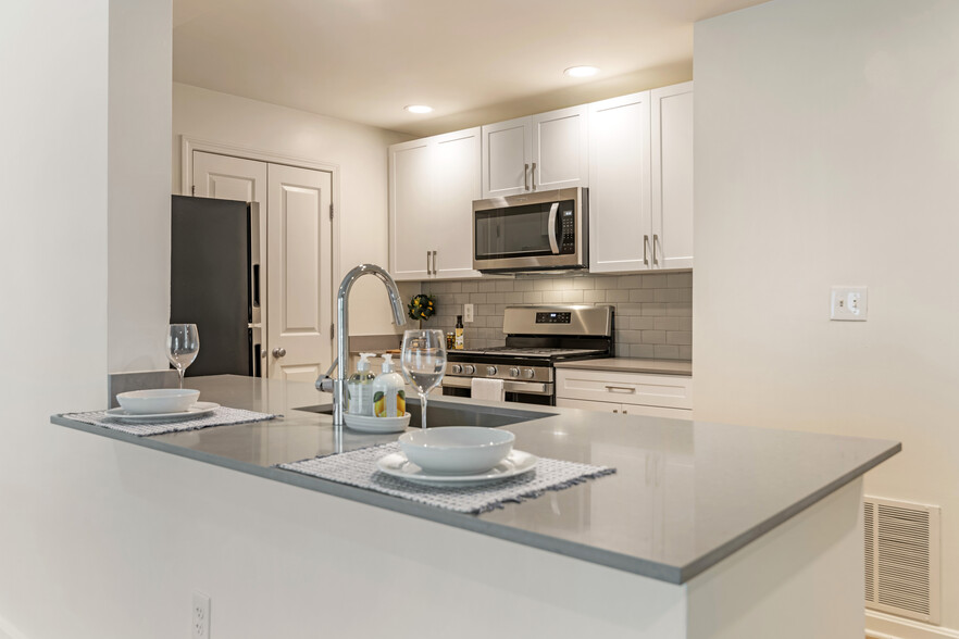 Renovated Package I kitchen with white cabinetry, grey quartz countertops, grey tile backsplash, stainless steel appliances, and hard surface plank flooring - Avalon at The Pinehills