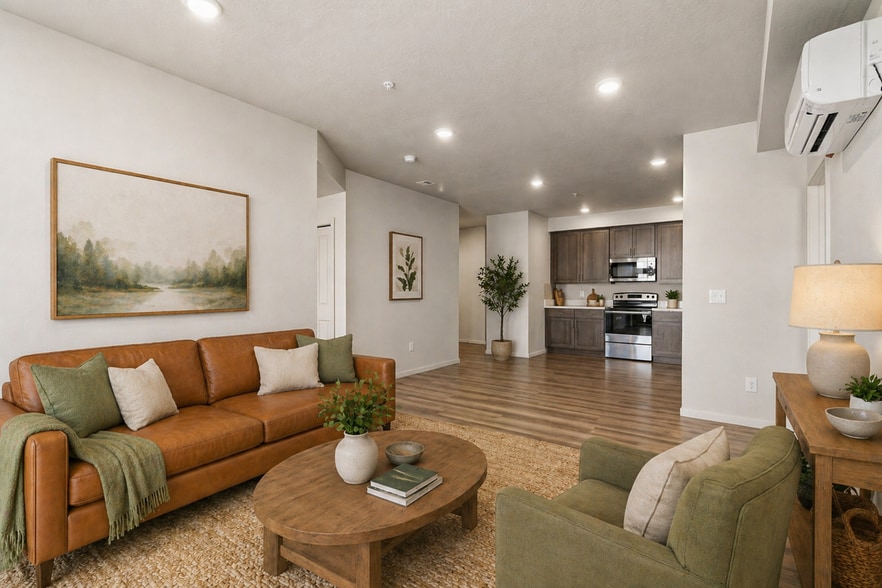 Modern open-concept living space with cozy brown leather sofa, greenery, and sleek kitchen featuring wood cabinetry. - Lofts at Garden District