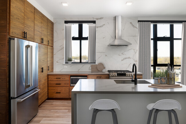 Kitchen with wood cabinetry, grey quartz countertops, marble backsplash, stainless steel appliances, and hard surface flooring - Avalon Hawk