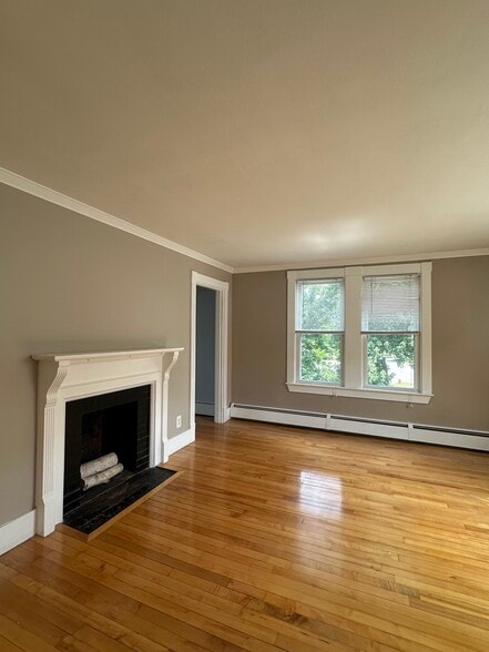 Bright, sunlit living room with decorative wood-burning fireplace and hardwood floors - 363 Concord Rd