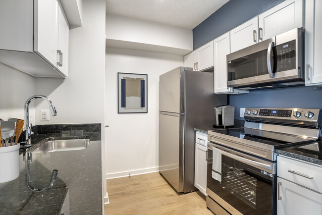 Renovated Package II kitchen with stainless steel appliances, white shaker cabinetry, dark speckled granite countertops, and hard surface flooring - AVA Ballston